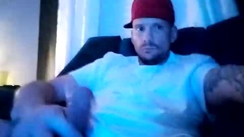 Media: Video of a man with a red cap and a white shirt, slightly blurred, in a dimly lit room with blue lighting, giving a serious look.