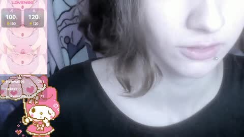 Media: A close-up video of a young woman with fair skin and wavy brown hair, wearing a black shirt. The background features a pink and white patterned wall with a virtual background overlay displaying a heart icon and \"LOVE ME\" text.