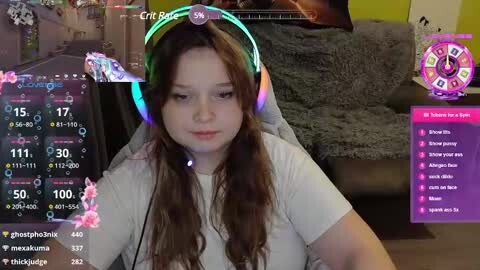 Media: Video of a young woman with long brown hair, wearing a headset, playing an online game. Background shows a cozy living room with a plush sofa.