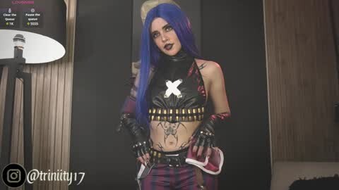 Media: Video of a woman with long blue hair, wearing a black leather crop top with a white cross, red and black plaid pants, and black fingerless gloves, standing in a dimly lit room.