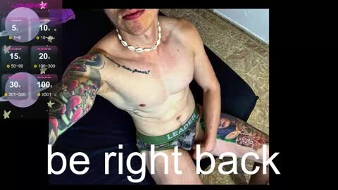 Media: Video of a shirtless man with a muscular build, wearing green boxer briefs, tattoos on his arm and leg, standing on a beige rug. Overlay reads \"be right back\" in white text.