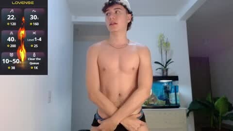 Media: Video of a shirtless young man with fair skin, black hair, and a slim build, wearing only black briefs, standing in a modern, minimalist room with a fish tank and plant.