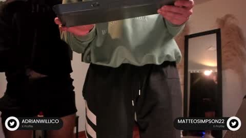 Media: Video of a person in a green sweatshirt and black pants, taking a selfie in a dimly lit room with a fur coat and a mirror in the background.