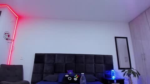 Media: Video of a modern bedroom with a dark gray, tufted headboard, red neon lighting, and a potted plant on the nightstand.