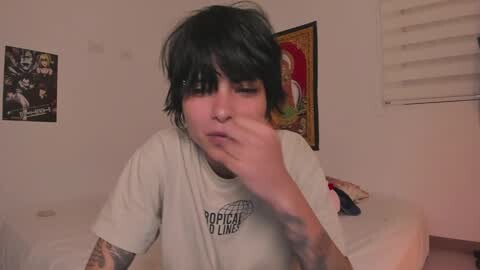 Media: A video of a person with short, dark hair and tattoos, wearing a \"Populair\" T-shirt, blowing their nose in a bedroom with posters and blinds.