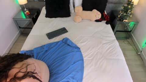 Media: Video of a man in a blue shirt sleeping on a white bed, surrounded by plush toys, including a large teddy bear and a red and black Santa Claus.