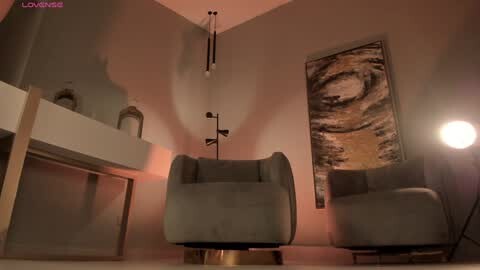 Media: Video of a minimalist, modern living room with gray upholstered armchairs, a beige sofa, a large abstract tiger painting, a floor lamp, and a white fireplace mantle. Warm, ambient lighting.