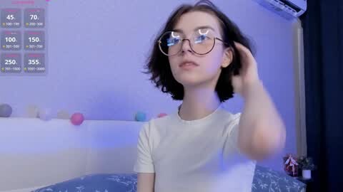 Media: A video of a young woman with short dark hair, wearing glasses and a white shirt, adjusting her hair in a dimly lit bathroom with a digital thermometer, blue accents, and a bathtub in the background.