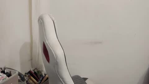 Media: A video of a white, upholstered chair with a curved back against a plain, off-white wall. The chair is positioned slightly to the left, and a cluttered desk with papers and a small trash can is visible in the background.