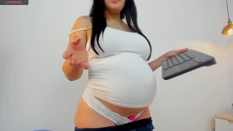 Media: Video of a pregnant woman with long black hair, wearing a white tank top and lace panties, giving a thumbs-up while holding a laptop.