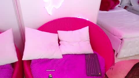 Media: Video of a bright, pink-walled bedroom with a large, round, wicker chair covered in a bright pink cushion, featuring two white pillows and a laptop on a purple blanket.