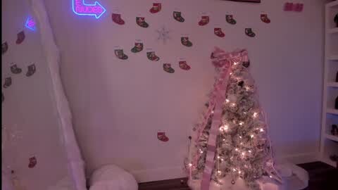 Media: Video of a cozy Christmas-themed room with a small, decorated tree adorned with pink ribbons and white lights, surrounded by red and green stockings.