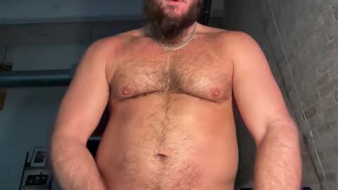 Media: Video of a shirtless, bearded, muscular white man with a hairy chest and belly. He wears a gold chain and stands in a dimly lit room with concrete walls and exposed pipes.