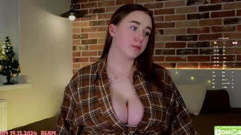 Media: Video of a fair-skinned woman with long auburn hair, wearing an unbuttoned plaid shirt revealing her large breasts. Background features a brick wall, Christmas tree, and a dimly lit room with a TV displaying a chat room.