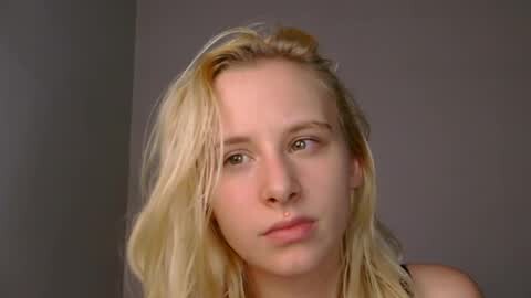 Media: A video of a young blonde woman with fair skin and straight hair, looking tired and pensive against a plain grey background. She appears to be wearing a black top.