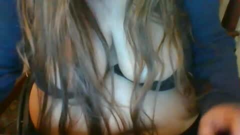 Media: A video shows a close-up of a woman's chest, with medium-sized breasts partially covered by a black bra. Her long, wavy blonde hair partially obscures her face. She is wearing a dark blue top.