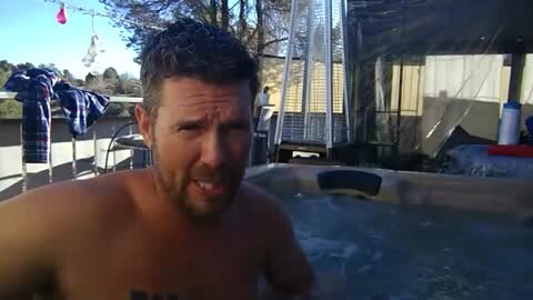Media: A video of a shirtless man with short dark hair and a beard, looking annoyed, sitting in a hot tub. Background includes a deck with a white fence and laundry hanging.