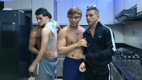 Media: Video of three shirtless men in a modern kitchen: one with a towel, one in blue shorts, and one in a black jacket.