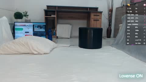 Media: A video of a minimalist bedroom with a large flat-screen TV, a wooden desk, and a black cylindrical stool; a virtual reality headset is placed on the bed.