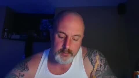 Media: Video of a middle-aged bald man with a white tank top and tattoos, eyes closed, in a dimly lit room with blue lighting.