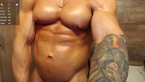 Media: Video of a nude, muscular, light-skinned person with small breasts, showing a detailed tattoo sleeve and a visible belly button, set against a wooden wall background.