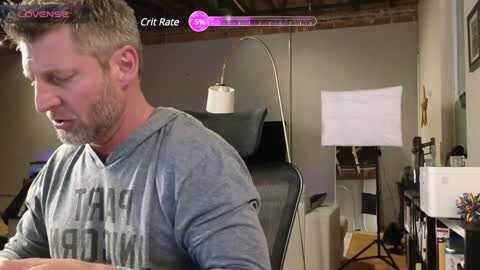 Media: Video of a middle-aged white man with short brown hair, wearing a gray \"Star Wars\" shirt, sitting at a desk in a cluttered room with a black office chair, whiteboard, and various office supplies.