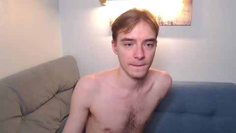 Media: Video of a young, shirtless white man with light brown hair, sitting on a blue couch in a dimly lit room.