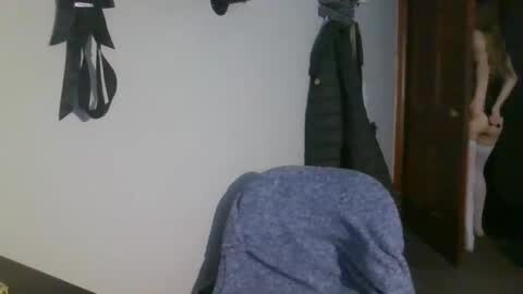 Media: Video of a man in a dark suit standing in a dimly lit room with a blue cloth draped over a chair, black silhouettes on the wall, and a partially open door.
