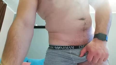 Media: Video of a light-skinned, shirtless man with a slightly paunchy stomach, wearing grey Armani underwear. He has a black smartwatch on his left wrist. Background shows a blue couch and part of a room with white walls.
