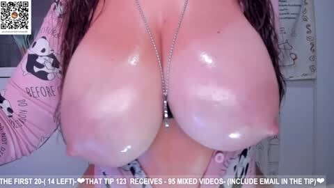 Media: Video of a woman with large, shiny, glistening breasts, wearing a pink long-sleeve shirt with panda prints, and a silver necklace. The background shows a bathroom with a white towel and text overlay.