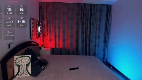 Media: Video of a dimly lit bedroom with a bed, a black remote control, and a digital clock displaying 15:10 on the wall. The room is bathed in red and blue LED lights, creating a vibrant yet mysterious ambiance.
