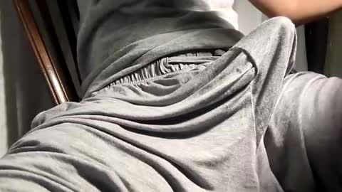 Media: A video shows a person's lower torso and legs wearing light gray, loose-fitting sweatpants with a drawstring, partially sitting on a wooden chair. The background is blurred, focusing on the fabric texture and casual attire.
