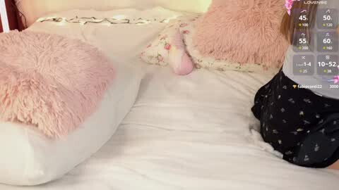 Media: Video of a plush white dog bed with a fluffy pink pillow and a white pillow with a floral pattern. A person's leg, wearing black pajamas with a white star pattern, is partially visible.