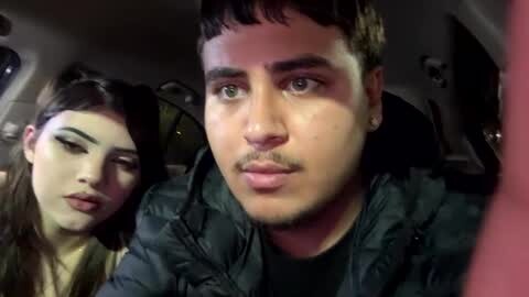 Media: Video of two young people in a car: a man with short dark hair in a black jacket, and a woman with long dark hair in a yellow sweater, both looking serious.