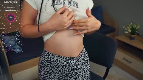 Media: A video of a light-skinned woman lifting her white crop top, revealing her midriff, wearing a leopard-print skirt in a modern, cozy living room.