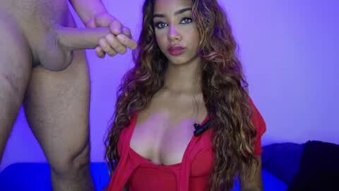 Media: A video of a Latina woman with long wavy hair and large breasts in a low-cut red dress, holding a man's erect penis, against a purple-lit background.