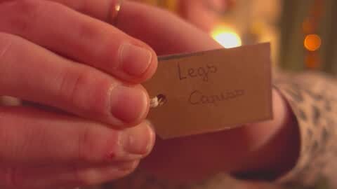 Media: A close-up video of a person's hand holding a small wooden sign labeled \"Legg\" and \"Contra.\" The background is softly blurred, featuring warm, ambient lighting and indistinct shapes.