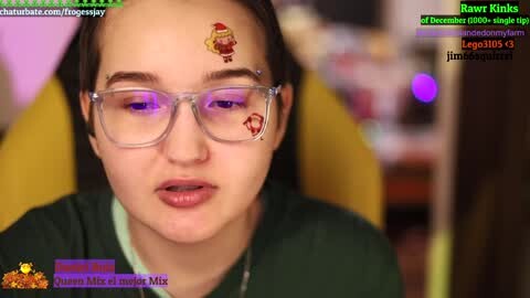 Media: Video of a young woman with light skin, brown hair, and glasses, wearing a green shirt. She has a festive face tattoo. Background is blurred. Overlayed text includes Twitch chat and streamer information.