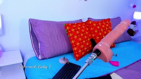 Media: Video of a purple sofa with a red pillow, a pink dildo on a blue cushion, and a silver vibrator on a white table, in a purple-themed room.