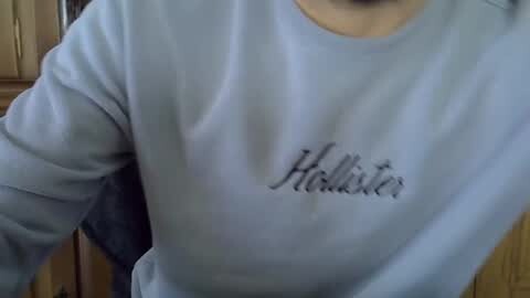 Media: Video of a person wearing a light blue Hollister sweatshirt with the brand name embroidered in black script. The person is indoors, with a wooden cabinet visible in the background.