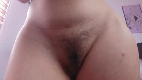 Media: A close-up video of a nude female torso with light skin tone, showing pubic hair, a natural body shape, and a small tattoo on the right side. Background includes a partially visible window and framed art on a white wall.
