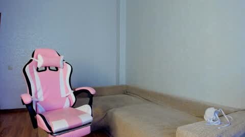 Media: A video of a minimalist living room with a pink gaming chair and beige sectional sofa, against light blue walls, featuring a white skull on the armrest.