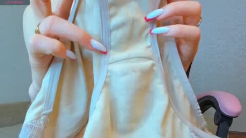 Media: A close-up video of a person's hands in a cream-colored sleeveless dress, with manicured nails painted in gradient colors. The background features a plain, light-colored wall and a pink office chair.