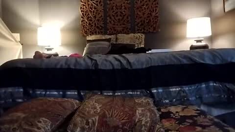 Media: Video of a cozy bedroom with a large bed, dark bedding, and ornate headboard; two bedside lamps casting warm light, and decorative pillows with intricate patterns.