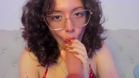 Media: A video of a light-skinned woman with curly dark hair and glasses, wearing a red bra, seductively licking a large, erect penis. She has a septum piercing and manicured nails.
