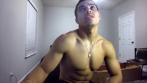 Media: Video of a shirtless, muscular young man with short dark hair, light skin, and a gold necklace, looking up in a dimly lit room with white walls, a window with blinds, and a closed door.