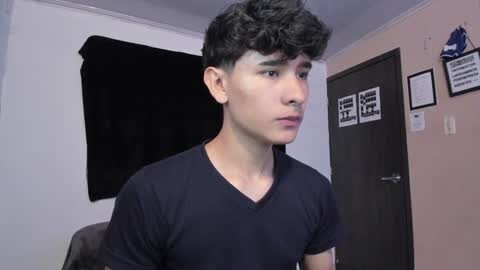 Media: Video of a young, curly-haired, fair-skinned male in a dark V-neck T-shirt, standing in a room with black curtains, white walls, and framed art.