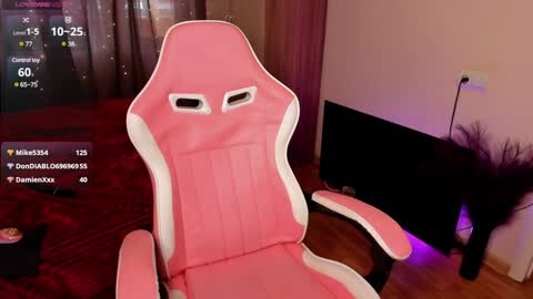 Media: Video of a pink gaming chair with white accents, positioned in a dimly lit room with a TV displaying a game interface and a digital clock.