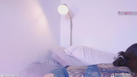 Media: A video of a dimly lit bedroom corner with a bed, a white lamp, and a partially visible person in a black jacket, leaning against the wall.