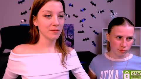 Media: Video of two young women in casual attire, one with an off-shoulder white top, the other in a blue t-shirt, in a room with Halloween decor and a gaming setup.